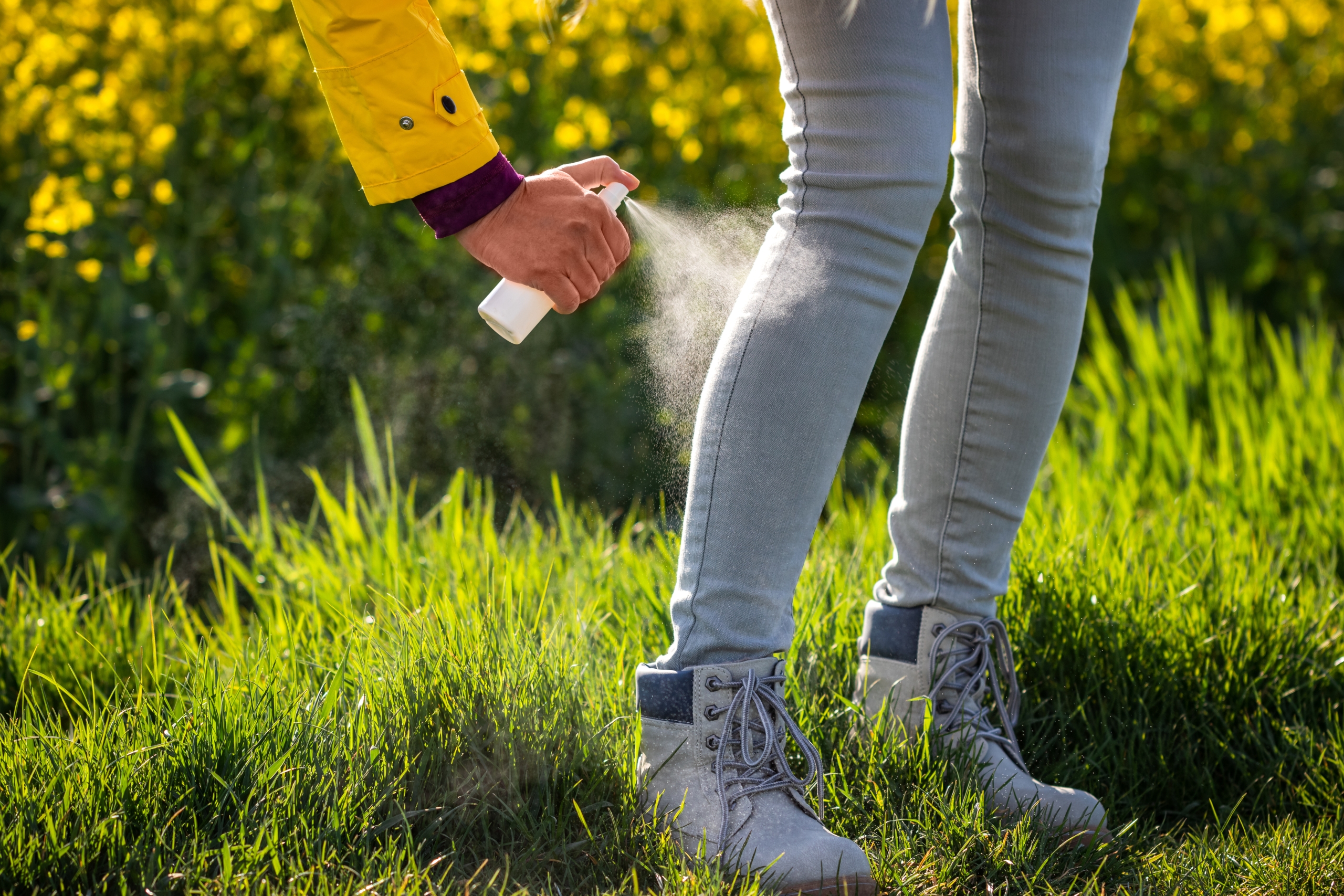 A person getting their pant legs sprayed with DEET.