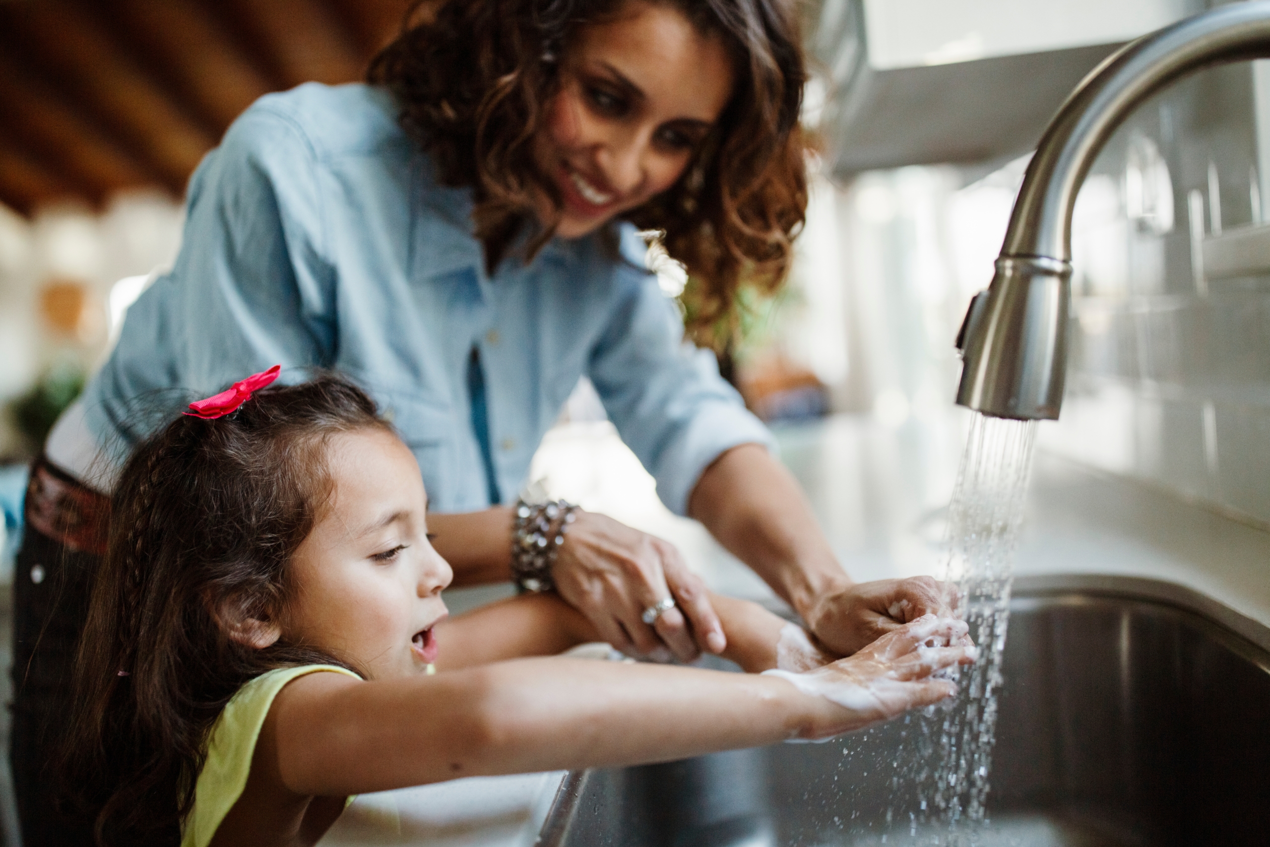 A mother helping her daughter wash her hands at the kitchen sink,