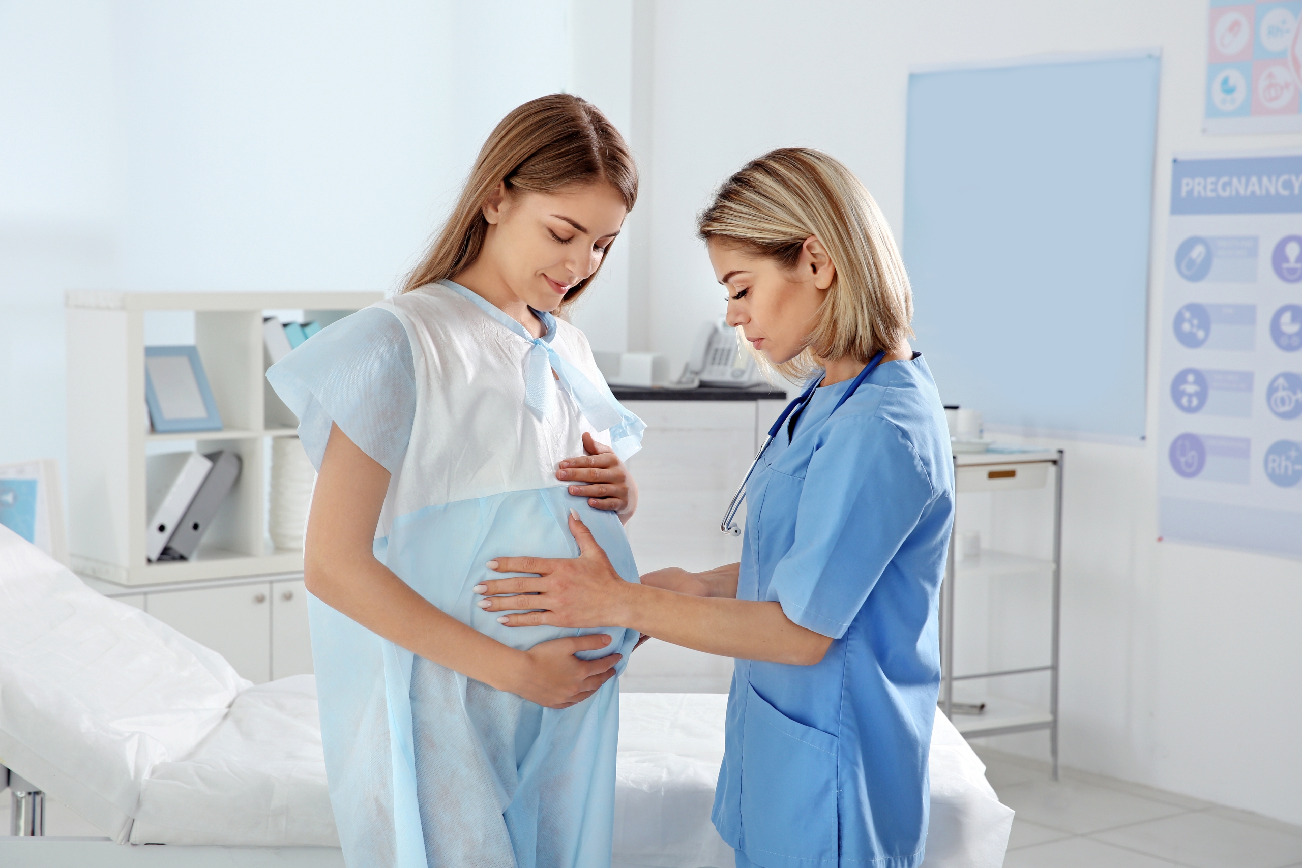 Pregnant woman standing while provider examines her belly.